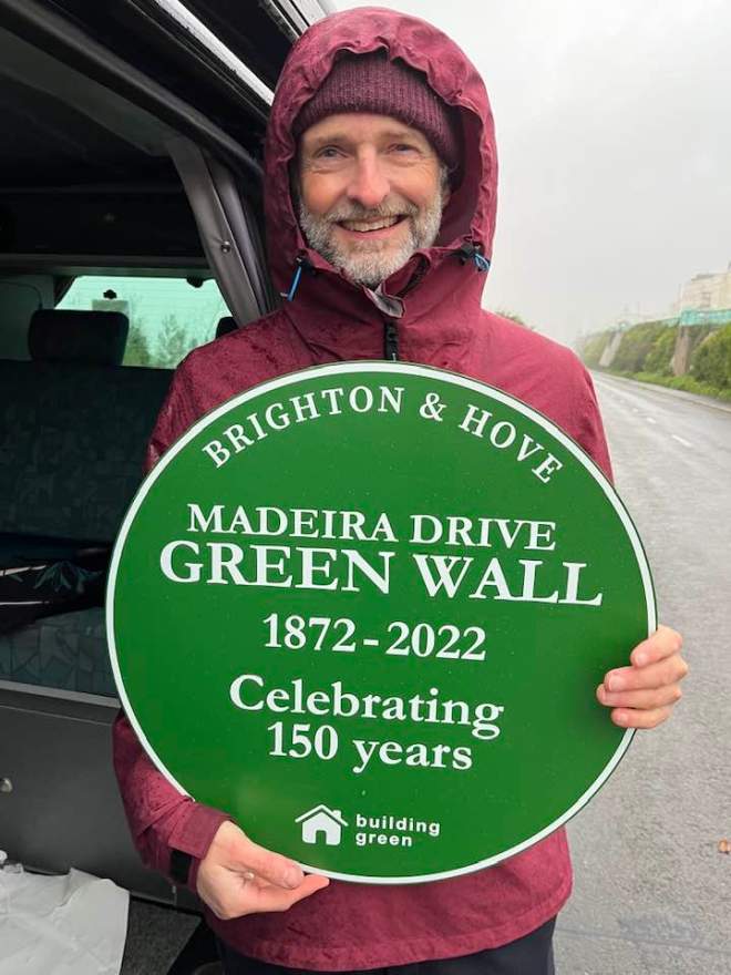 man with beard and green plaque commemorating 150 years of madeira drive green wall brighton